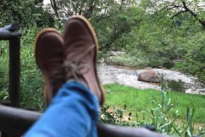 uma pessoa com os pés num banco ao lado de um rio em Lions Rock Rapids - Luxury Tented Camp em Hazyview
