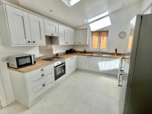 eine Küche mit weißen Schränken, einer Spüle und einer Mikrowelle in der Unterkunft Rye Court Cottage and Annex Central Hemsley in Helmsley