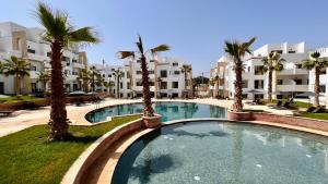 a swimming pool with palm trees in front of a building at Dominium Residence in Agadir
