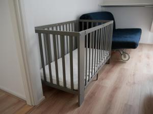 a crib and a blue chair in a room at Jonas - Luxe appartement naast de duinen in Oosterend