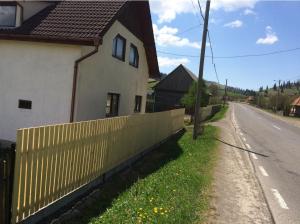 a white house with a fence next to a road at Karacsony Guest House in Lunca de Sus