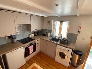 a kitchen with white cabinets and a washer and dryer at Honeysuckle Cottage by The Sea in Mousehole