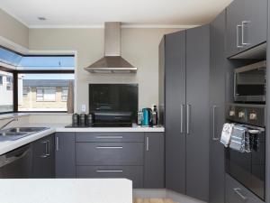 a kitchen with gray cabinets and a sink at At The Bay - Mt Maunganui Holiday Home in Matapihi