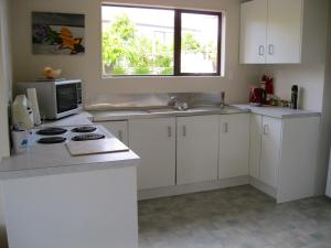 a kitchen with white cabinets and a stove and a window at Cooks Beach Gem - Cooks Beach Holiday Home in Cooks Beach