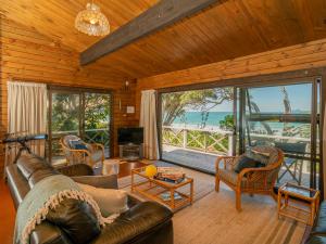 a living room with a leather couch and a large window at Norma's Place - Simpsons Beach Bach in Whitianga