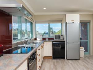 a kitchen with stainless steel appliances and windows at Tuis Nest - Bowentown Holiday Home in Waihi Beach
