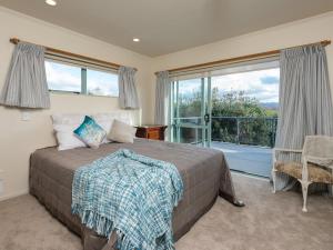 a bedroom with a bed and a large window at Tuis Nest - Bowentown Holiday Home in Waihi Beach