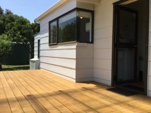 a house with a wooden deck next to a building at Ronas - Whiritoa Beach Bach in Whiritoa