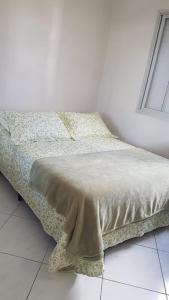 a bed in a white room with a bedspread on it at QUARTO TOP no CENTR0 com Cama Box de casal - acomoda até 2 pessoas - Home Office - WIFI - Smart TV com Apps Youtube - Cozinha - banheiro - Sala de Estar - Apto compartilhado com Anfitriões experientes em hospedar - Superhost no BnB 5 estrelas in Criciúma