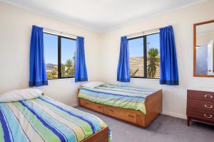 two beds in a bedroom with blue curtains at Room for The Family - Bowentown Bach in Waihi Beach