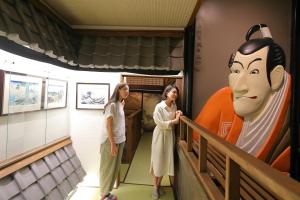 dos mujeres de pie en una escalera junto a una estatua de una máscara en Hidatakayama Ukiyoe INN Garon - Vacation STAY 12320v, en Takayama
