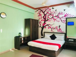 a bedroom with a bed and a tree with pink flowers at STAYMAKER Prakash International in Gonikoppal
