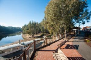 a walkway next to a river with a bench at Luxury on the Esplanade in Echuca