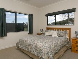 a bedroom with a bed and two windows at Lake Magic - Motuoapa Holiday Home in Turangi