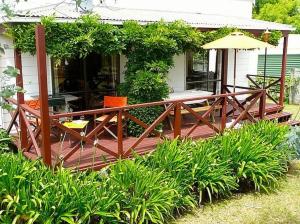 a wooden deck with a table and chairs on a house at Cute Cottage - Cooks Beach Bach in Cooks Beach
