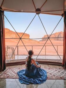 a young girl sitting on the floor looking out at the desert at Bubble RumCamp in Wadi Rum