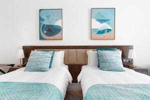 2 Betten in einem Hotelzimmer mit Gemälden an der Wand in der Unterkunft Ultimate Stay Avani next to Palm Jumeirah in Dubai