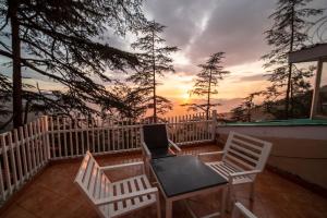 西姆拉的住宿－Holiday In Homestay，阳台上配有两把椅子和一张桌子,享有日落美景