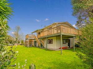 a house with a deck on a yard at Oyster Bach - Cooks Beach Bach in Cooks Beach