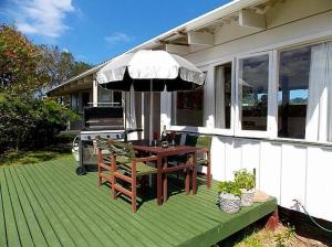 a patio with a table and an umbrella on a house at Hibiscus Cottage - Whangamata Bach in Whangamata