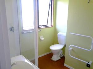 a bathroom with a toilet and a tub and a window at The Sands - Matarangi Holiday House in Matarangi