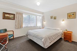 een slaapkamer met een bed, een stoel en een raam bij At The Mount - Mt Maunganui Holiday Home in Mount Maunganui