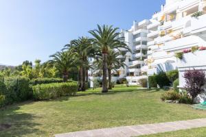 a garden in front of a building with palm trees at Moderno piso con piscina cerca del campo de golf - Quetzal 54 in Marbella