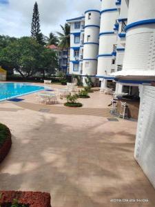 ein großes Apartmenthaus mit einem Pool, Tischen und Stühlen in der Unterkunft ARY Royal Palms - 1 BHK in Benaulim