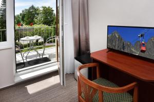 a room with a desk with a television and a balcony at APLEND Hotel Lujza Major in Vysoke Tatry - Tatranska Lomnica.
