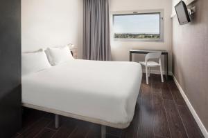 a bedroom with a white bed and a table and a window at B&B HOTEL Albacete in Albacete