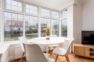 a dining room with a white table and chairs and windows at Wellington View - Donnini Apartments in Ayr