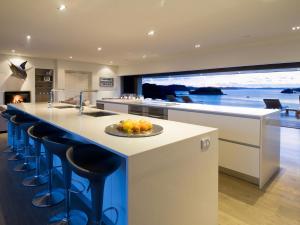 a kitchen with a island with bar stools and a large window at Oke Beach House - Rawhiti Luxury in Rawhiti