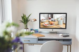 a computer monitor sitting on a desk with a plate of food at Waves - Duplex Apartment Stoke Fleming in Stoke Fleming