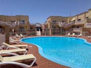 a large swimming pool with lounge chairs in front of buildings at Las Arenas caleta de fuste in Caleta De Fuste