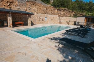 a swimming pool with chairs next to a stone wall at River huts Zrmanja in Obrovac