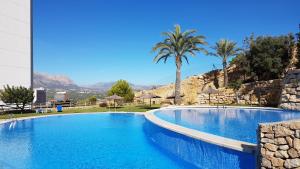 a large blue swimming pool with palm trees and mountains at Apartamento con terraza privada y vistas al mar in Benidorm