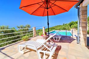 a red umbrella and a white chair on a patio at Holiday Home Zule in Žrnovo