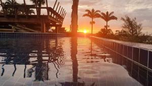 a swimming pool with a sunset in the background at Hotel Pousada Casacolina in Búzios