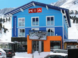 un bâtiment bleu et orange avec des voitures garées dans la neige dans l'établissement MIA Appartements - non-serviced Appartements, à Obertauern