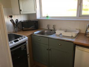 a kitchen with a sink and a stove and a microwave at Widemouth Waves Holiday Chalet in Poundstock