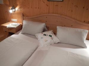 ein weißes Bett mit zwei Kissen und einer Holzwand in der Unterkunft Jörgleggerhof in Nikolsdorf