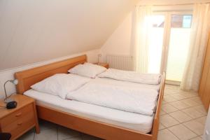- une chambre avec un lit doté de draps blancs et une fenêtre dans l'établissement Nordlicht Greetsiel, à Greetsiel