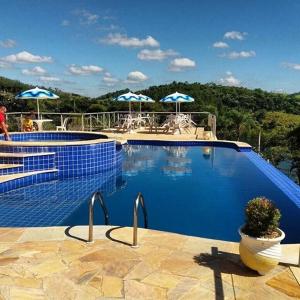 a blue swimming pool with umbrellas and chairs at Recanto Apoena in Santa Isabel