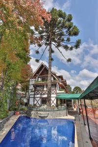 a swimming pool with a tree in front of a house at Le Suisse Elegance Hotel in Campos do Jordão