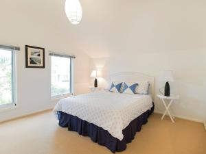 a white bedroom with a bed and two windows at Evergreen Beach House in Inverloch