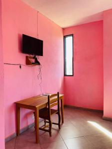 Habitación con mesa de madera y pared de color rosa. en LE JAVA en Antsakomboena