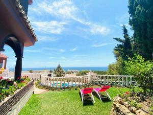 twee rode stoelen in het gras bij een zwembad bij Villa Geneviève Costa del Sol in Mijas Costa