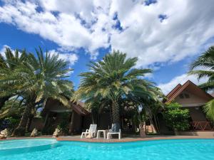 una piscina con palmeras y 2 sillas blancas en La-or Resort, en Hua Hin