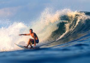 a man riding a wave on a surfboard in the ocean at Anantara Uluwatu Bali Resort in Uluwatu