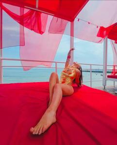 una mujer tendida en una cama roja bajo un paraguas en Club House Arkadia Beach en Odesa